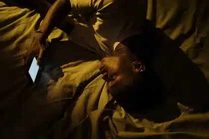 Ein Mann liegt wach im Bett, kann nicht einschlafen, Wecker auf dem Nachttisch sichtbar